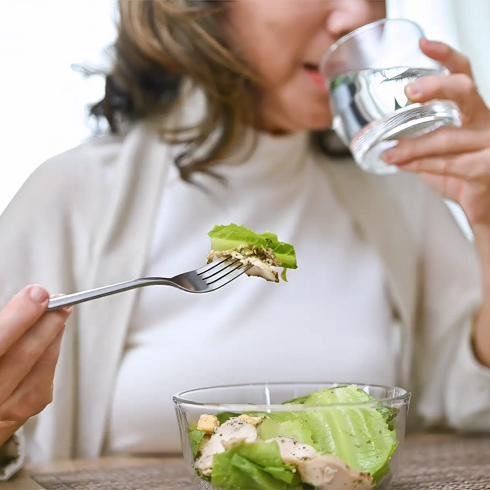 Healthy and happy Asian-aged eating salad bowl and drinking water 