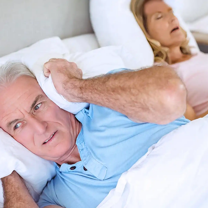 Senior man lying on bed and covering his ears with pillow in bedroom